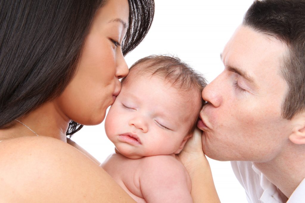 A mother and father both kissing their newborn baby.